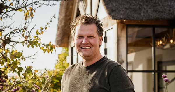 Een trotse, glimlachende man met kort krullend haar en donkergroen t-shirt.